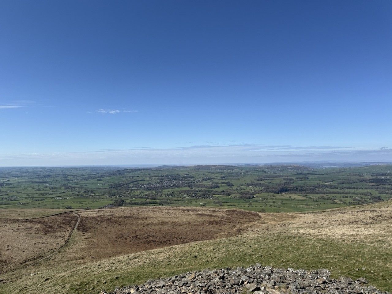 Photo taken from the top of the cairn on Brownthwaite Pike. The sky is a bright blue and there are rolling fields and a valley in the distance.